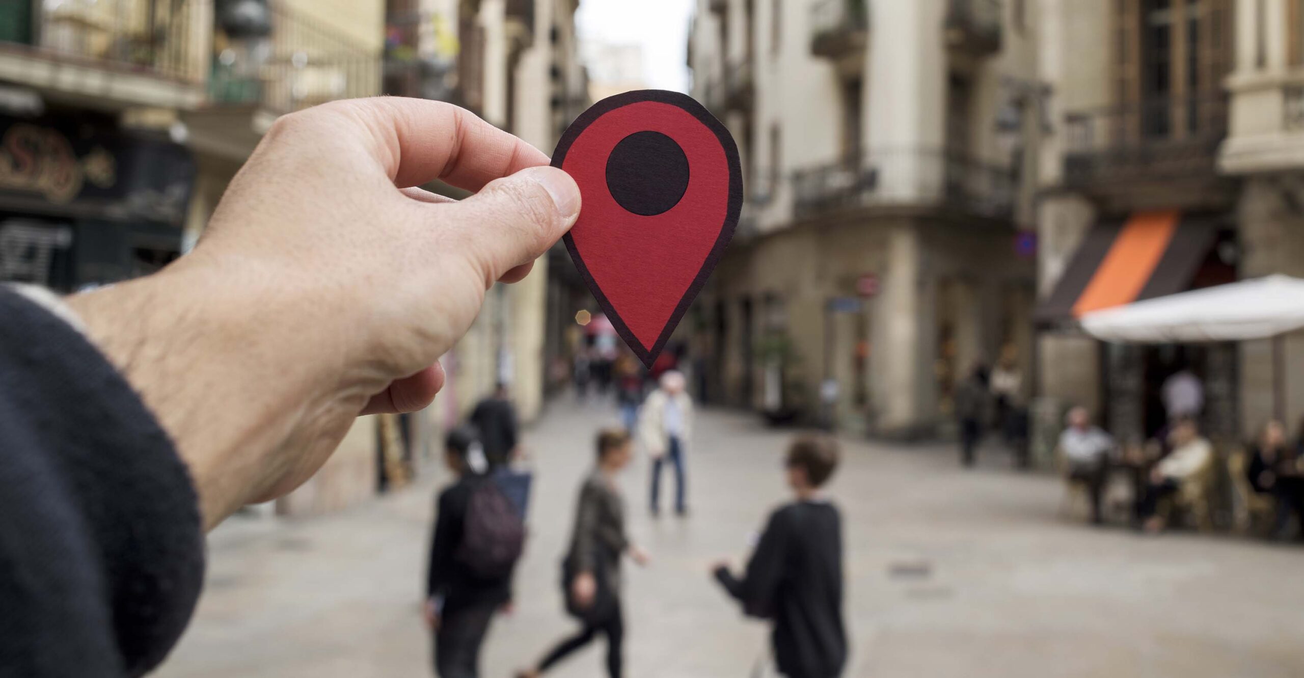 Primer plano de la mano de una persona con un marcador de sitio rojo en el casco antiguo de una ciudad