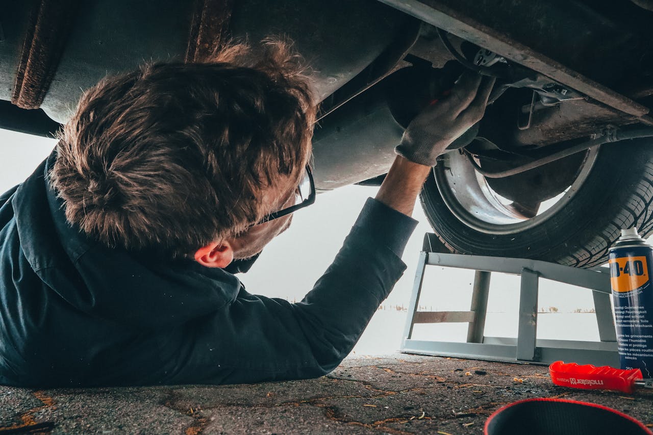 Junge unter einem Auto, das eine Reparatur durchführt.